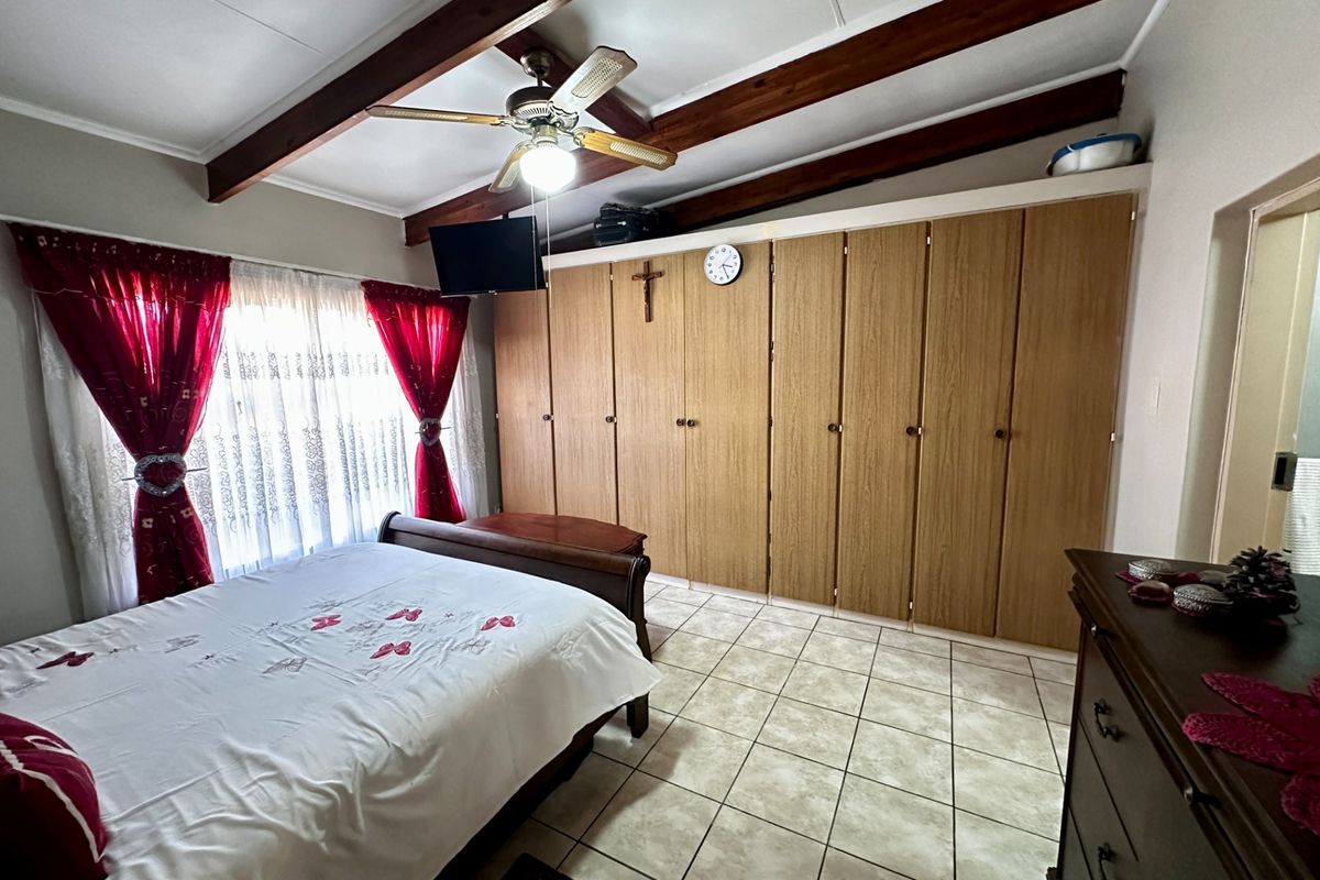 A bedroom featuring tiled flooring, exposed timber ceiling beams, a ceiling fan, and extensive built-in wooden cupboards for storage.