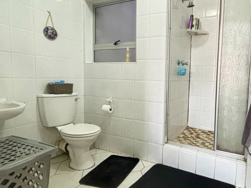 A functional bathroom featuring a shower enclosure, toilet, and tiled finishes. The space would benefit from modern updates to fixtures and tiling.