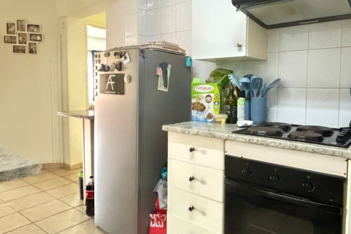 A functional kitchen featuring built-in cabinetry, an electric oven and hob, extractor fan, and tiled flooring with a neutral splashback.