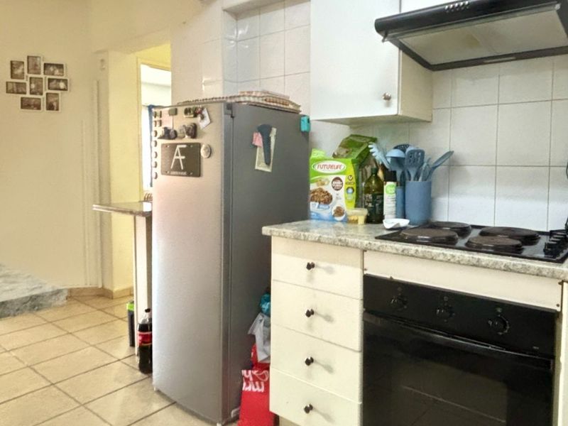 A functional kitchen featuring built-in cabinetry, an electric oven and hob, extractor fan, and tiled flooring with a neutral splashback.