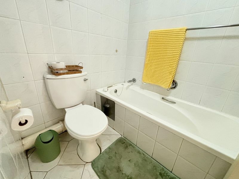 A functional bathroom featuring a built-in bathtub, toilet, and full-height wall tiling. The space would benefit from modern updates to finishes and fixtures.