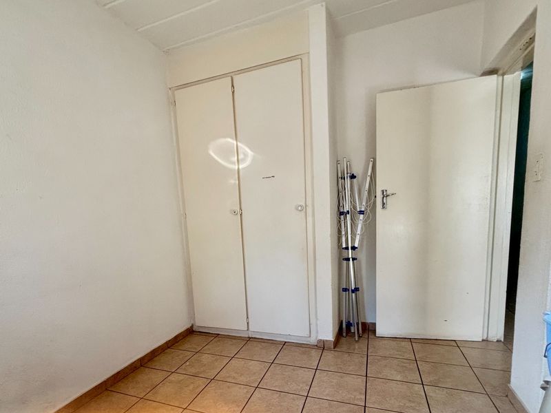 A simple, empty bedroom featuring tiled flooring and a built-in cupboard, offering a clean canvas for personalization.