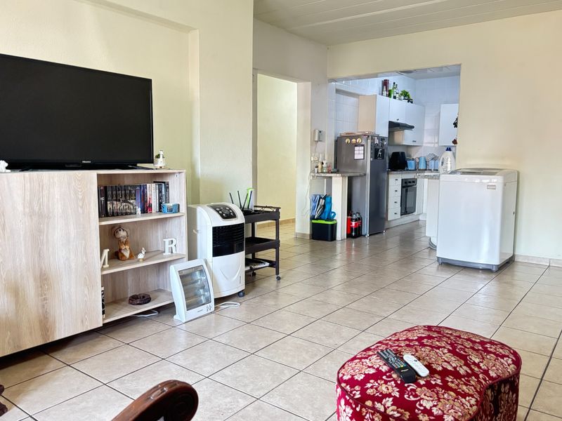 Open plan living area flowing into a functional kitchen with tiled flooring and built-in cabinetry.