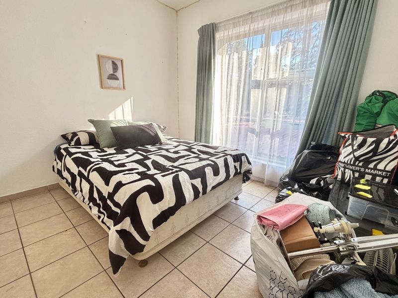 A bedroom featuring tiled flooring and a large window with curtain tracks, requiring minor cosmetic updates to the walls and ceiling.