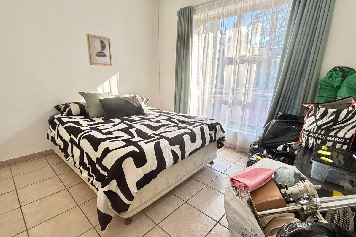 A bedroom featuring tiled flooring and a large window with curtain tracks, requiring minor cosmetic updates to the walls and ceiling.