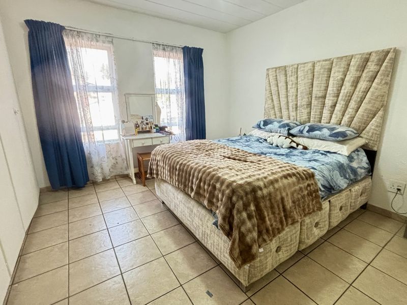 A bedroom featuring tiled flooring and dual windows, providing a functional space with neutral wall finishes.