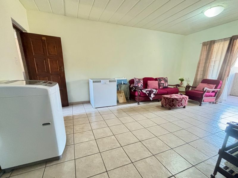 A spacious living area featuring neutral tiled flooring and a panelled ceiling, offering a functional layout with direct access to an outdoor space.