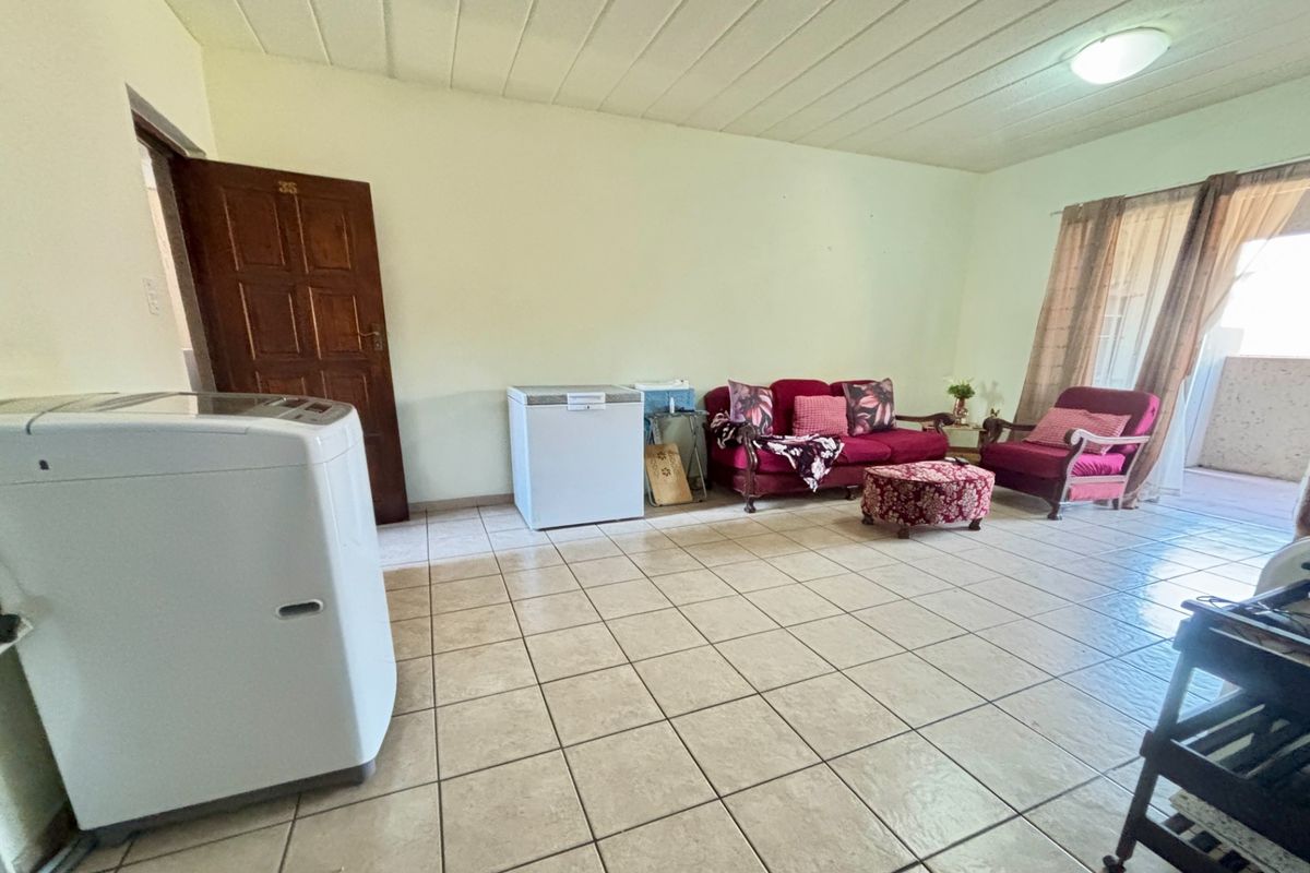 A spacious living area featuring neutral tiled flooring and a panelled ceiling, offering a functional layout with direct access to an outdoor space.