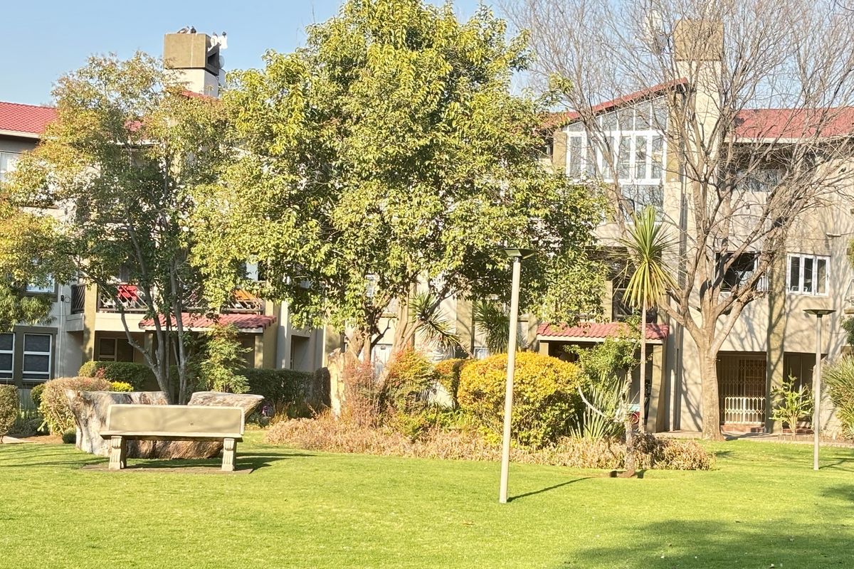 A view of the rear exterior of the townhouse complex, featuring a well-maintained communal garden with mature trees and lawn.