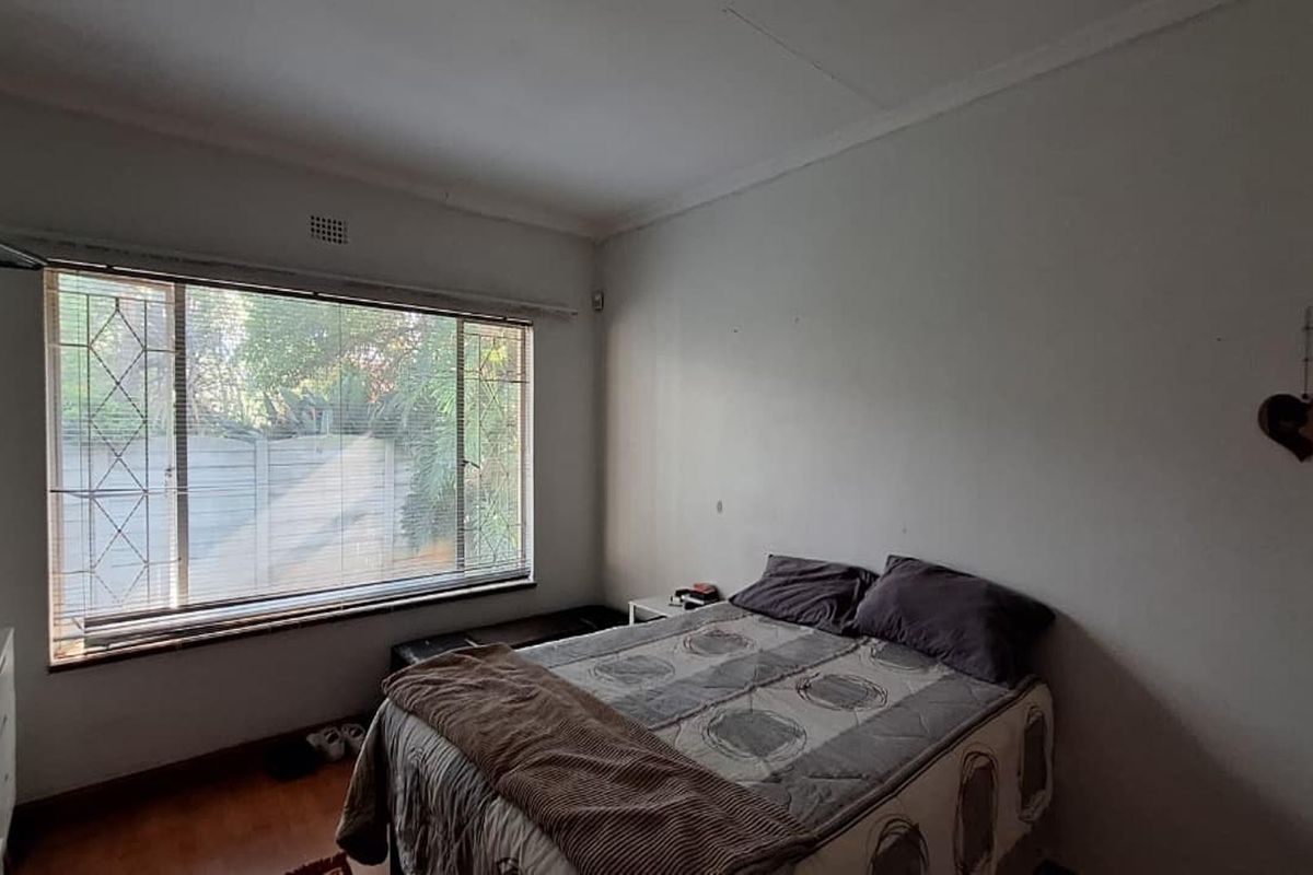 A bedroom featuring laminate flooring, security burglar bars on the window, and standard ceiling cornicing.