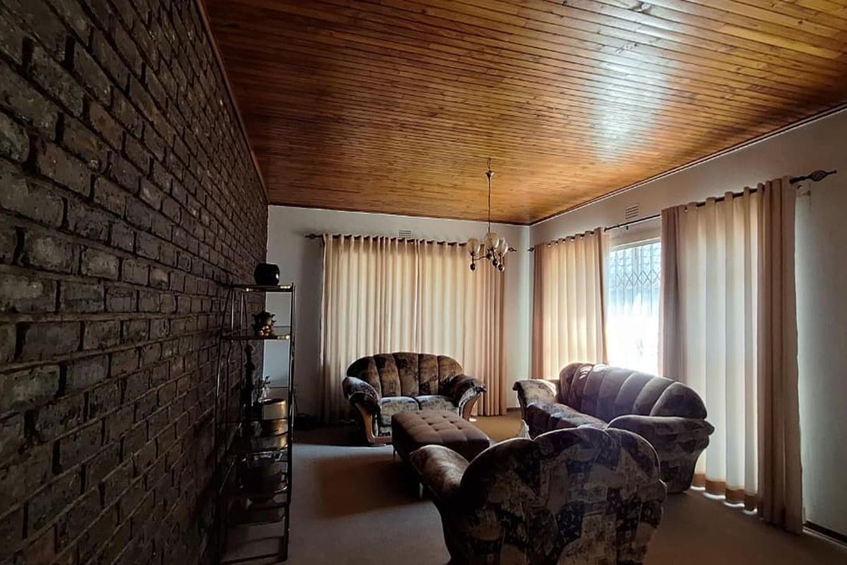 Spacious living room featuring a distinctive exposed brick feature wall and a warm timber tongue and groove ceiling.