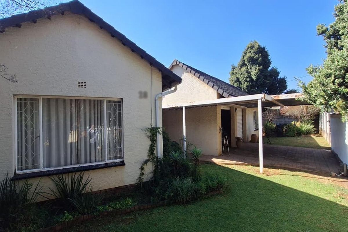 Rear view of the property featuring a covered patio area, paved driveway, and established garden space.
