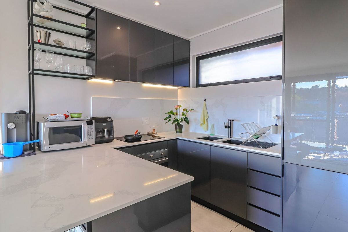 Modern kitchen featuring sleek dark glossy cabinetry, stone countertops, integrated appliances, and stylish under-cabinet lighting in a clean, contemporary layout.