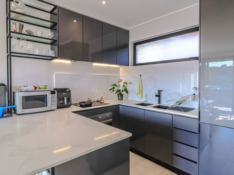 Modern kitchen featuring sleek dark glossy cabinetry, stone countertops, integrated appliances, and stylish under-cabinet lighting in a clean, contemporary layout.