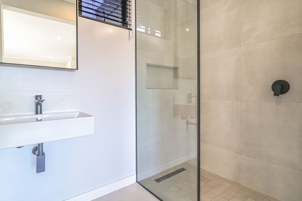 Modern bathroom featuring a wall-mounted basin, frameless glass shower with black hardware, built-in niche, and neutral large-format tiling.