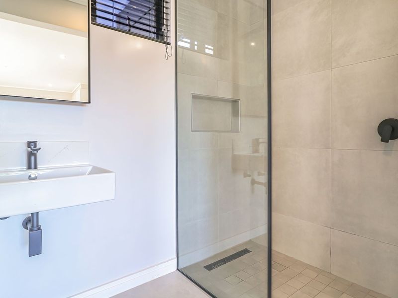 Modern bathroom featuring a wall-mounted basin, frameless glass shower with black hardware, built-in niche, and neutral large-format tiling.