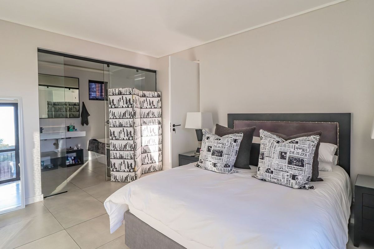 Spacious bedroom featuring neutral tones, tiled flooring, and a modern glass-partitioned en-suite bathroom, creating an open and contemporary living space.