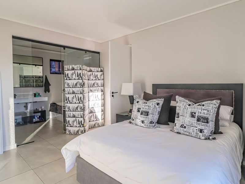 Spacious bedroom featuring neutral tones, tiled flooring, and a modern glass-partitioned en-suite bathroom, creating an open and contemporary living space.