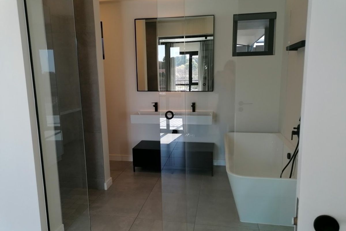 Modern bathroom featuring a sleek freestanding bathtub, double vanity with black matte fixtures, and a spacious glass-enclosed shower with contemporary tiling.