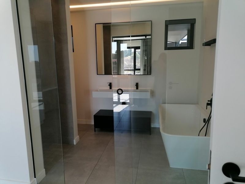 Modern bathroom featuring a sleek freestanding bathtub, double vanity with black matte fixtures, and a spacious glass-enclosed shower with contemporary tiling.