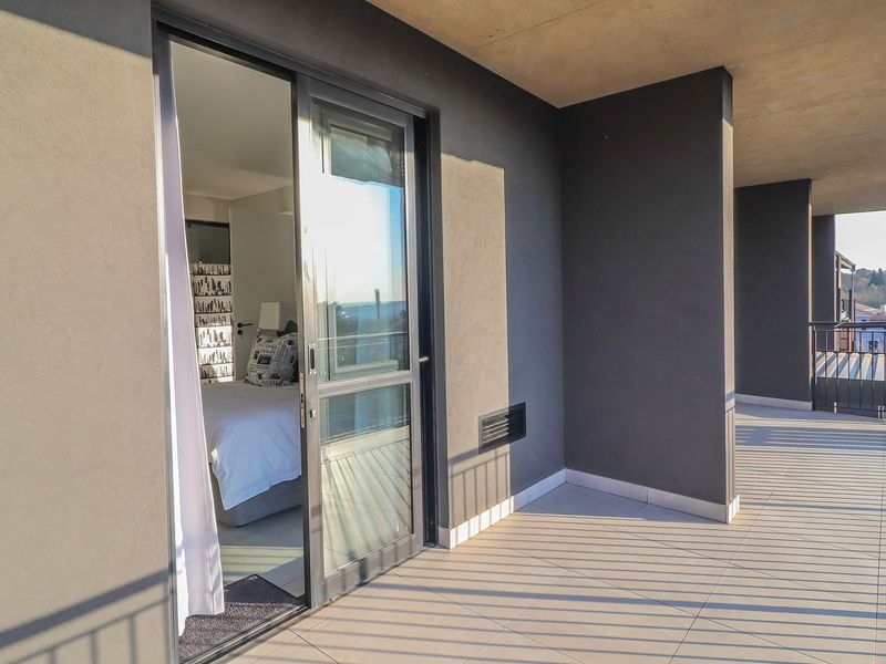 A spacious covered balcony with modern tiled flooring, metal railings, and direct access to the bedroom through a sliding glass door.