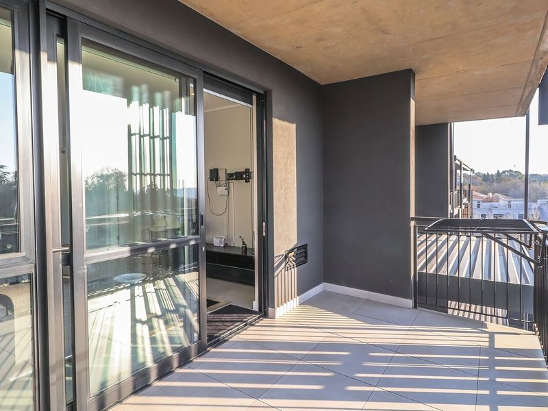 A modern covered balcony featuring tiled flooring, metal railings, and large sliding glass doors providing access to the interior living space.