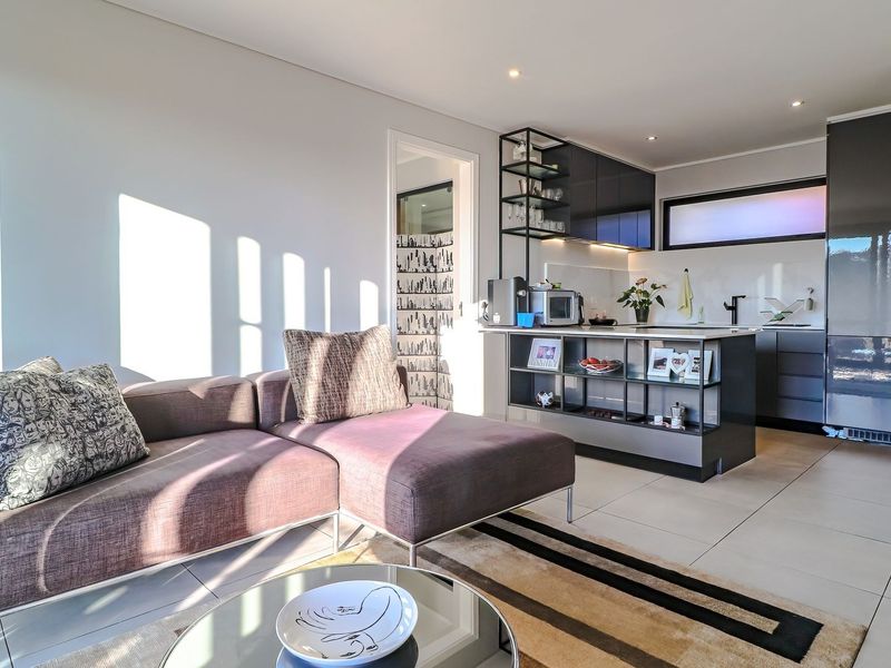 A bright open-plan living area featuring a modern kitchen with sleek cabinetry, a functional island, and neutral tiled flooring throughout.