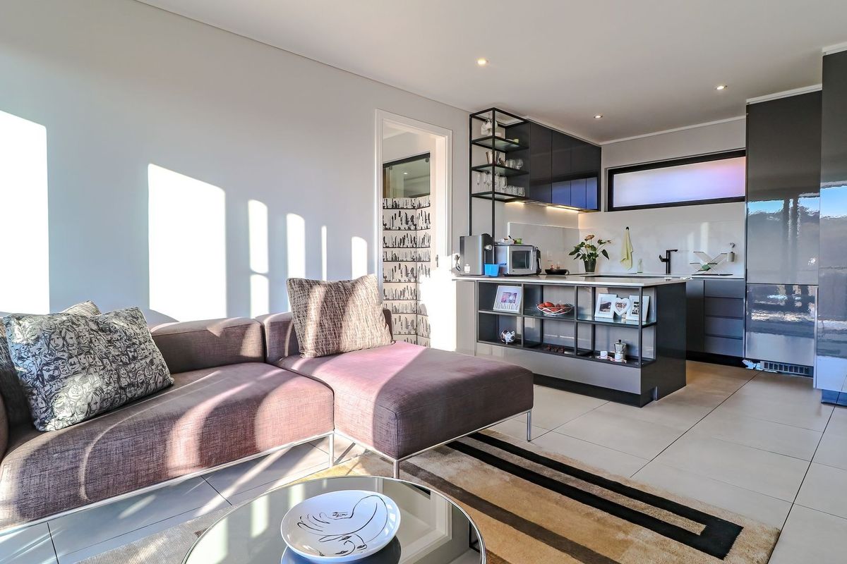 A bright open-plan living area featuring a modern kitchen with sleek cabinetry, a functional island, and neutral tiled flooring throughout.