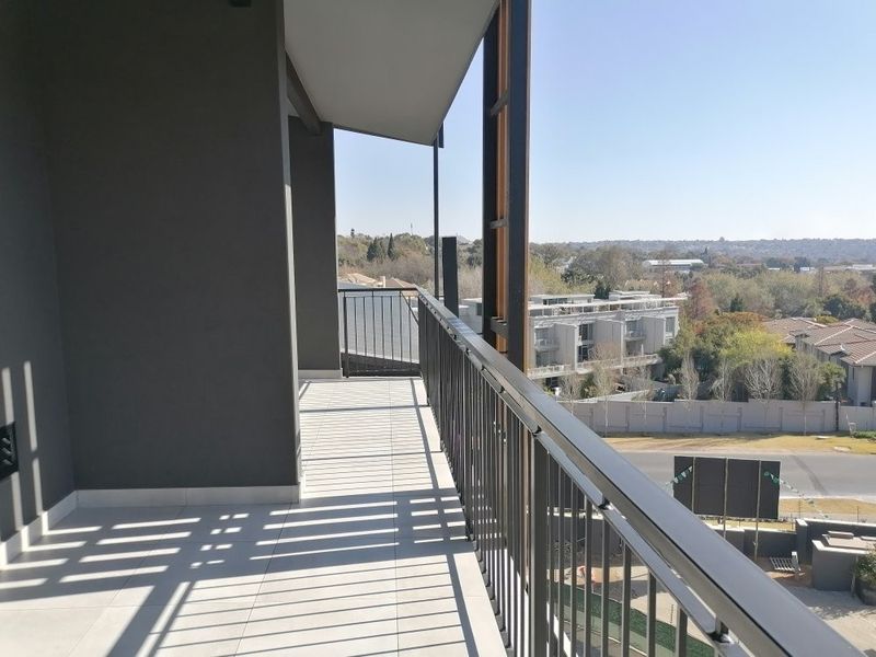 A spacious, modern covered balcony featuring tiled flooring and a sleek metal balustrade, offering elevated views of the surrounding neighborhood.