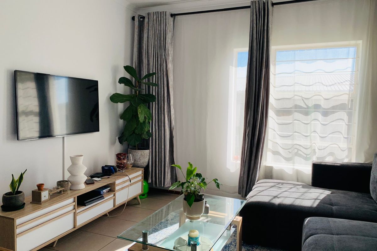 A bright and comfortable living room featuring tiled flooring and large windows with curtain tracks, creating a welcoming space for relaxation.