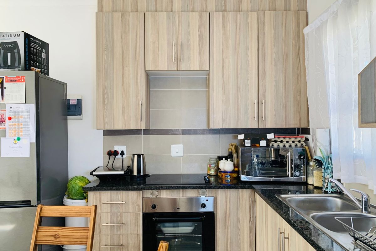 A functional kitchen featuring light wood-grain cabinetry, dark granite countertops, a built-in oven, electric hob, and a double sink with tiled backsplash.