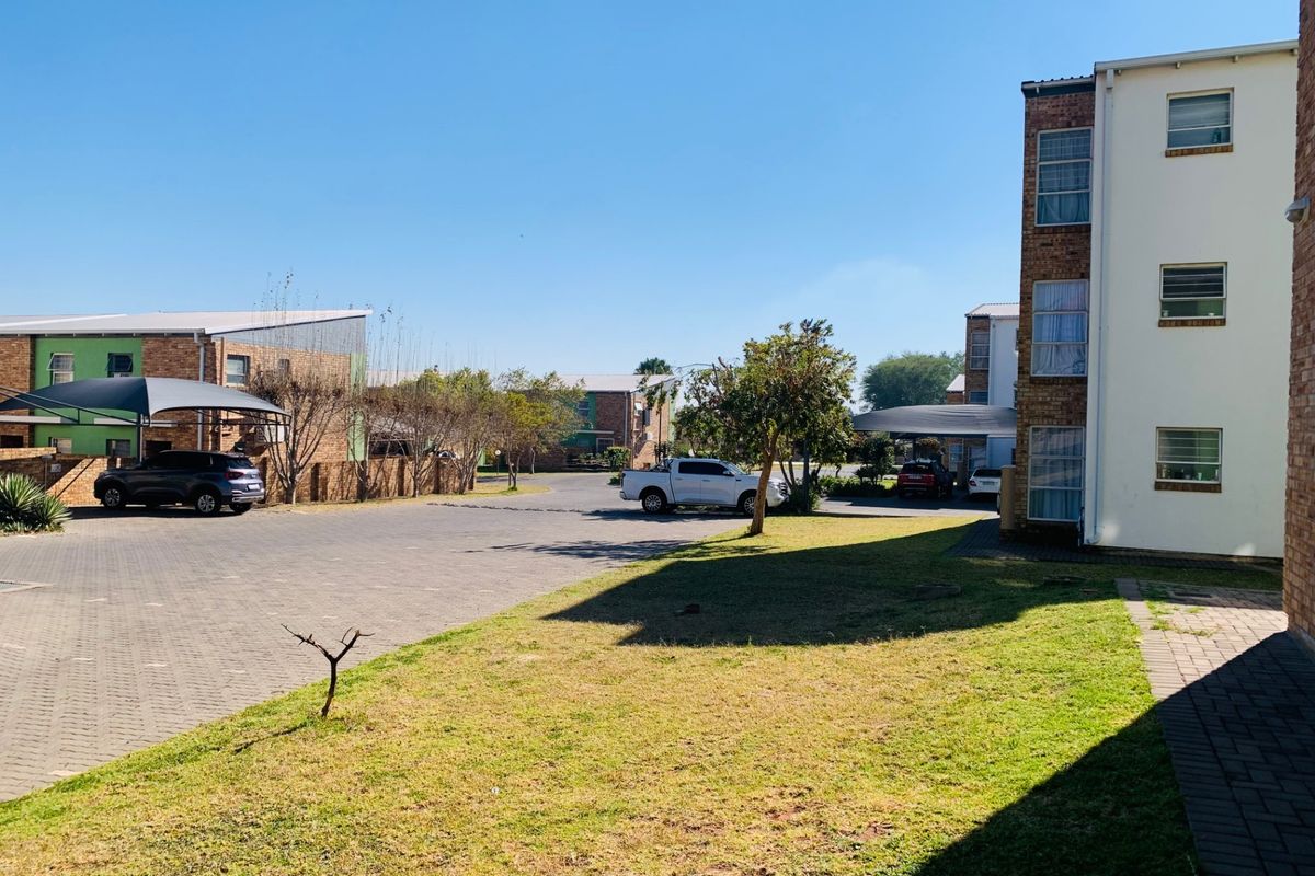 Exterior view of an apartment complex featuring paved parking areas, carports, and landscaped lawn space between residential buildings.