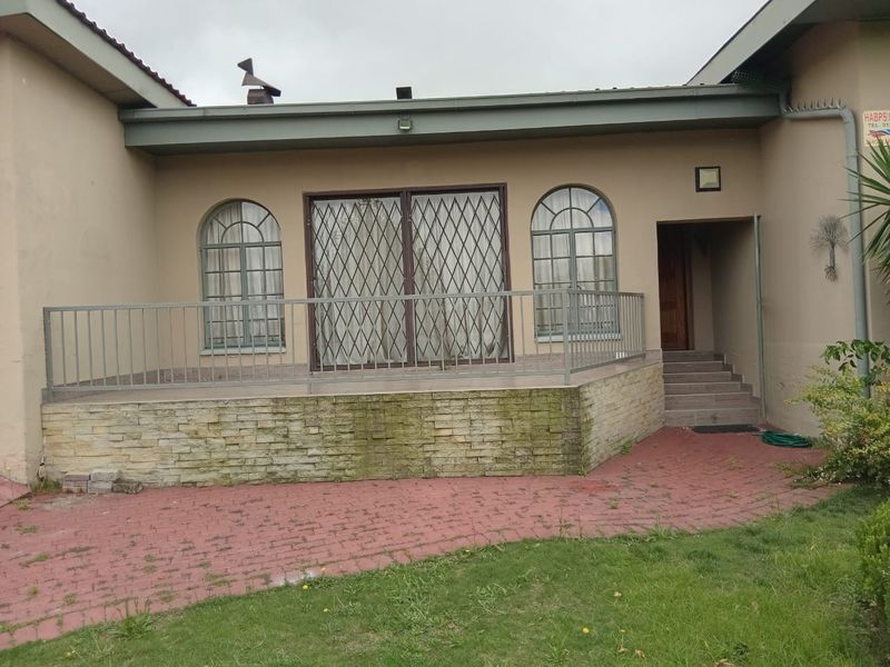 Rear exterior view featuring a raised patio with stone cladding, metal security gates, and arched windows, leading to a paved garden area.