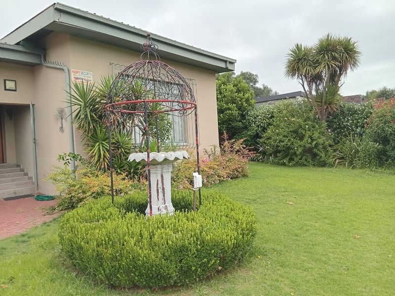 Front exterior view of the house featuring a landscaped garden, paved entrance walkway, and security signage on the building facade.