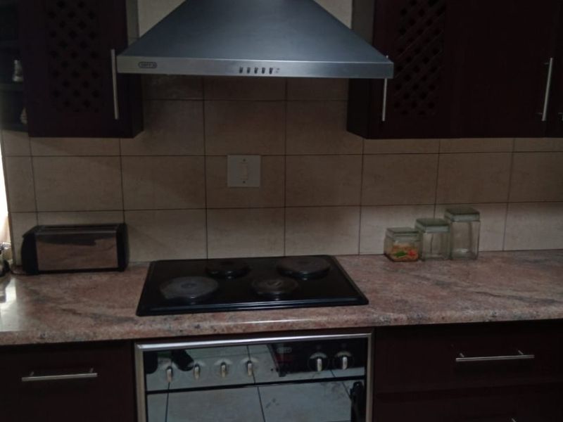A functional kitchen area featuring dark wood cabinetry, stone countertops, a built-in oven, electric hob, and a stainless steel extractor fan.