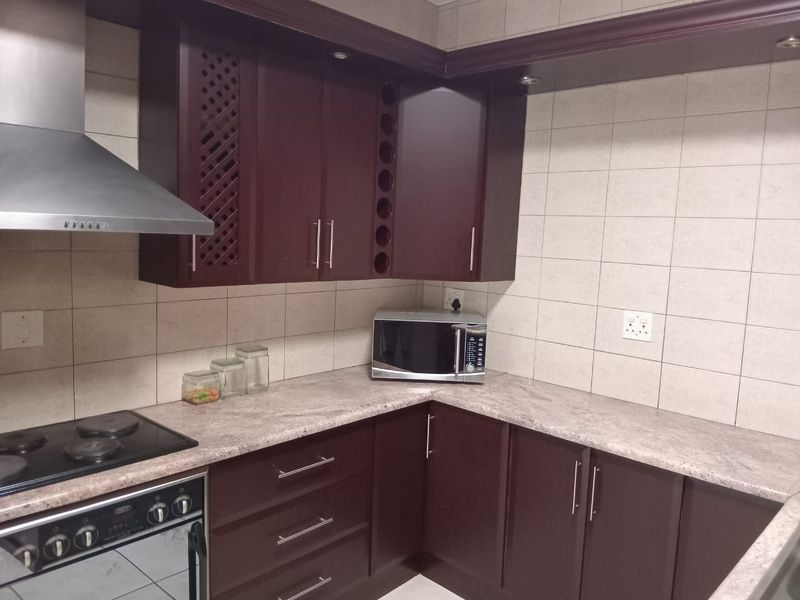 A functional kitchen featuring dark wood cabinetry, stone countertops, a built-in oven with ceramic hob, and a stainless steel extractor fan.