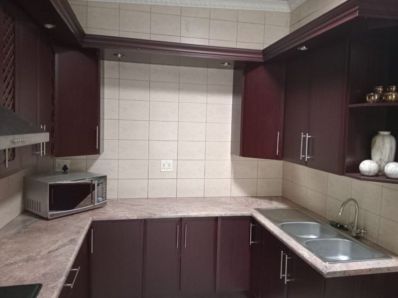 A functional kitchen featuring dark wood-finish cabinetry, laminate countertops, a double stainless steel sink, and tiled backsplash.