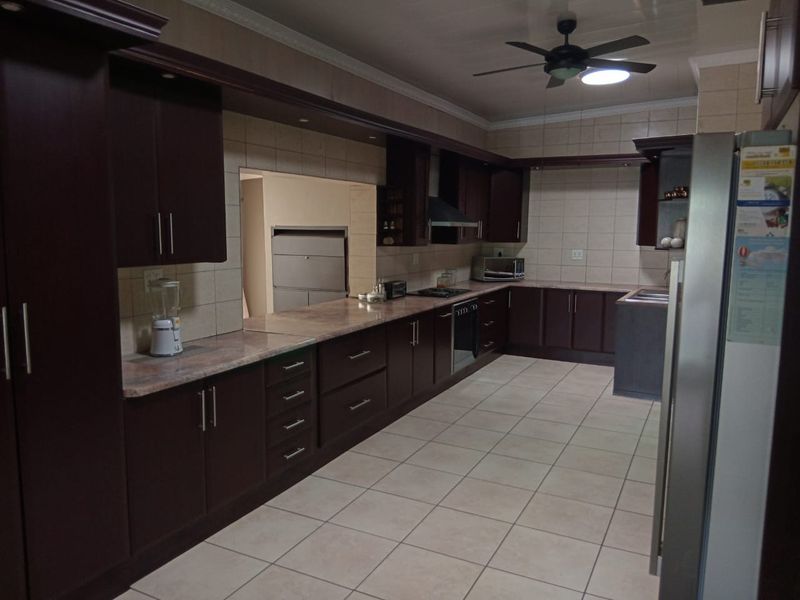 Spacious kitchen featuring dark wood cabinetry, stone countertops, tiled flooring, and integrated appliances, offering a functional layout with ample storage space.