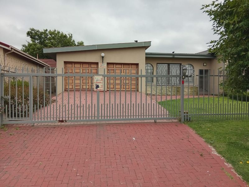 Front view of a single-story house featuring a double garage, paved driveway, and secure perimeter fencing with security gates.