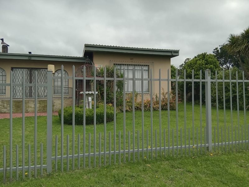Front view of a single-story house featuring a lawn, metal security fencing, and security bars on the windows.