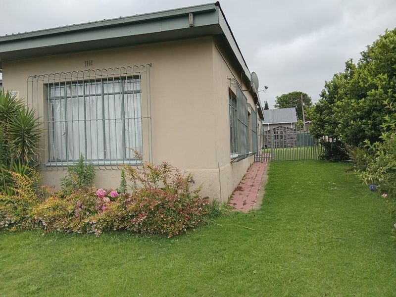 A view of the rear exterior of the house featuring a garden, paved walkway, and security bars on the windows.