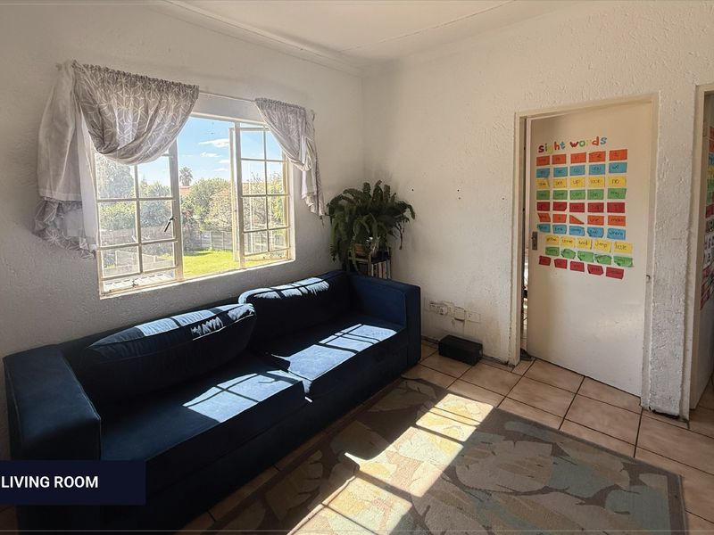 A living room featuring tiled flooring and a casement window with natural light, requiring cosmetic updates to the walls and finishes.