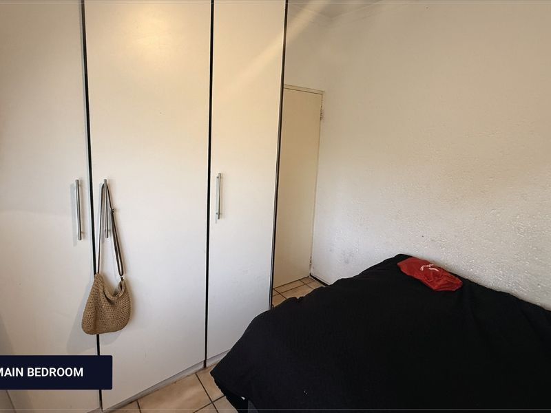 A bedroom featuring built-in cupboards and tiled flooring, requiring minor cosmetic updates to the wall finishes.