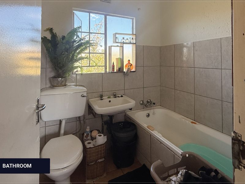 A compact bathroom featuring a standard bathtub, wall-mounted basin, and toilet with tiled wall finishes.