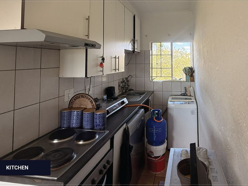 Compact kitchen featuring built-in cabinetry, electric hob, extractor fan, and stainless steel sink, with tiled backsplash and window for natural light.