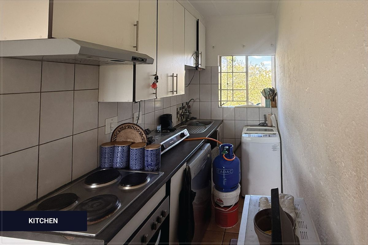 Compact kitchen featuring built-in cabinetry, electric hob, extractor fan, and stainless steel sink, with tiled backsplash and window for natural light.