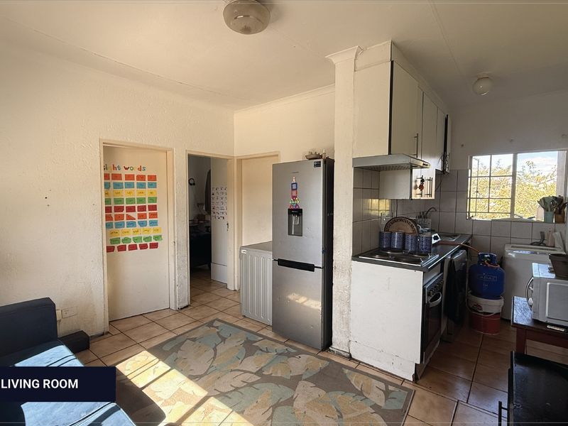 Open plan living and kitchen area featuring tiled flooring, built-in cabinetry, and integrated cooking appliances, offering a functional layout with potential for modernization.