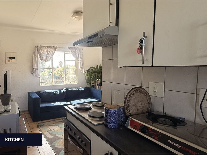 Open-plan kitchen and living area featuring built-in cabinetry, electric hob, extractor fan, and tiled flooring, offering a functional layout for daily living.