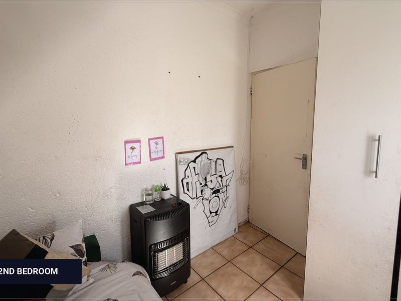 A compact second bedroom featuring tiled flooring and a built-in cupboard, requiring cosmetic updates to the wall finishes.