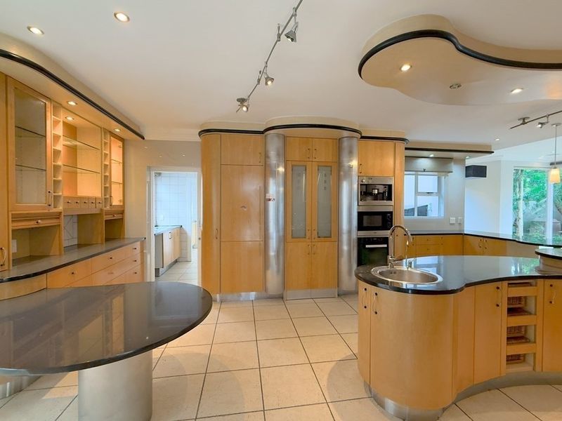 Spacious kitchen featuring custom curved cabinetry, stone countertops, integrated appliances, and a central island with a secondary sink.
